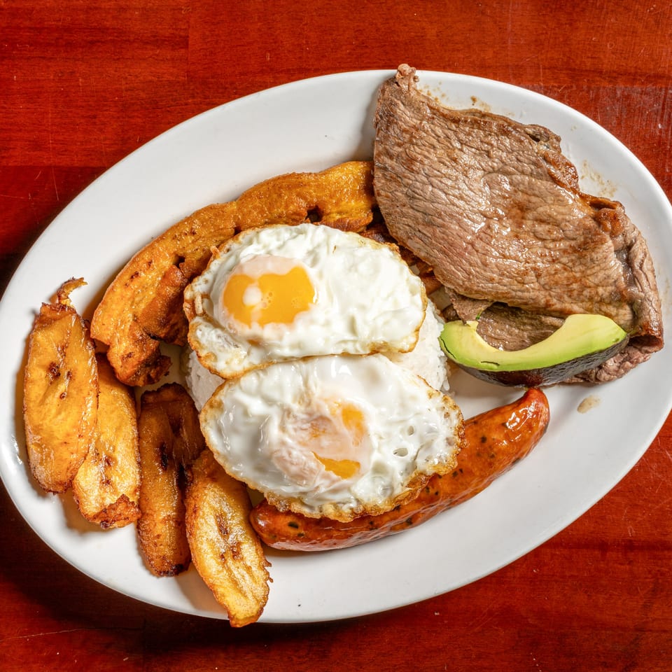 Cuban breakfast plate with steak, fried eggs, plantains, sausage, rice, and avocado.