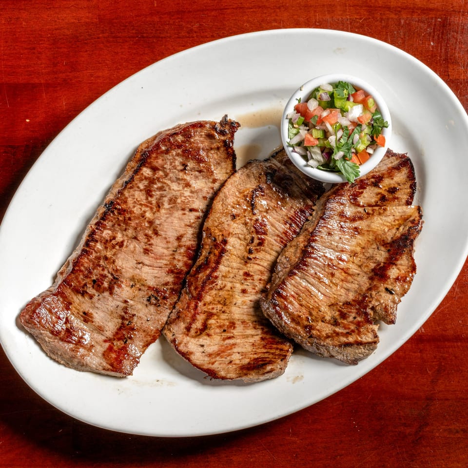 Three grilled Cuban steaks with a side of fresh pico de gallo on a white plate.