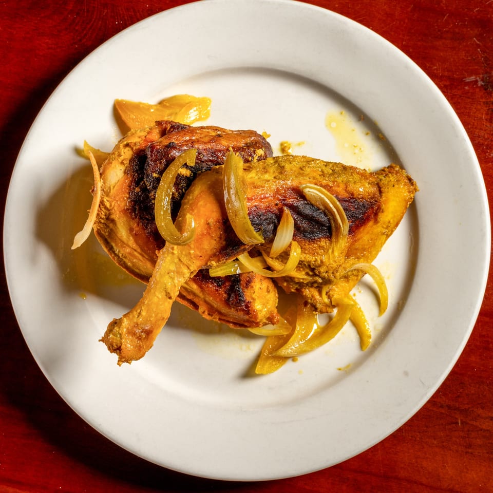 Cuban-style roasted chicken leg and thigh with sautéed onions and peppers on a white plate.
