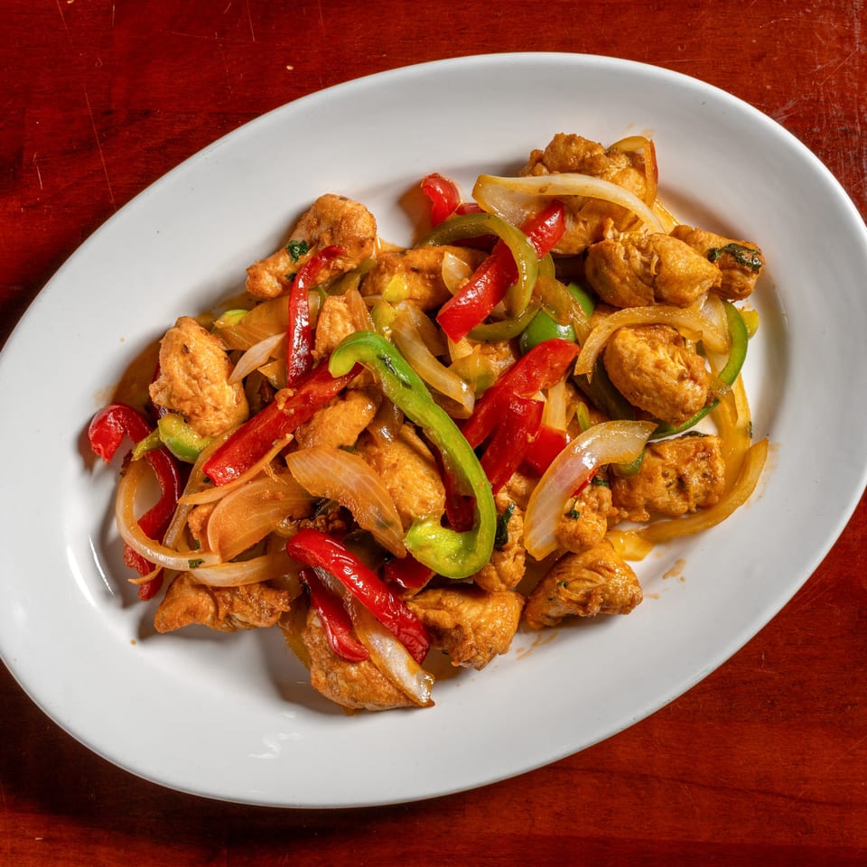 Cuban chicken stir-fry with red and green bell peppers and onions on a white oval plate.