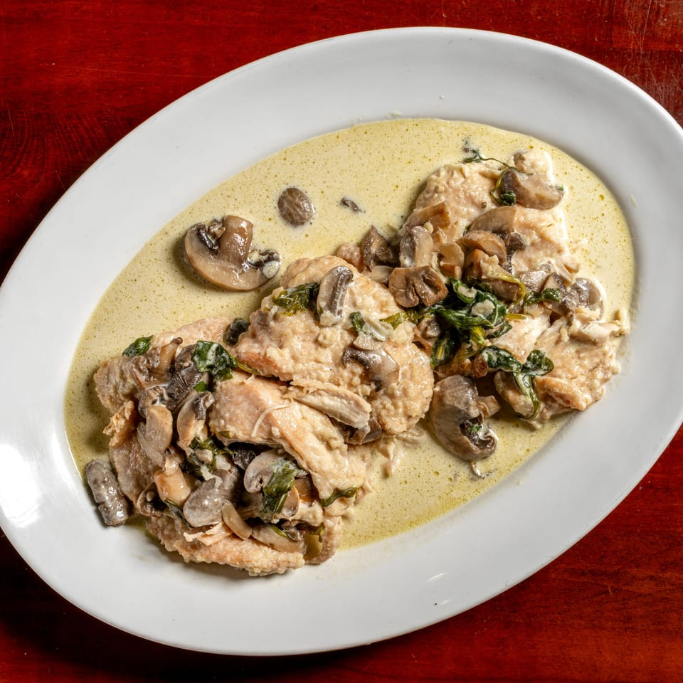 Chicken breast pieces in a creamy mushroom sauce with spinach, served on a white oval plate.