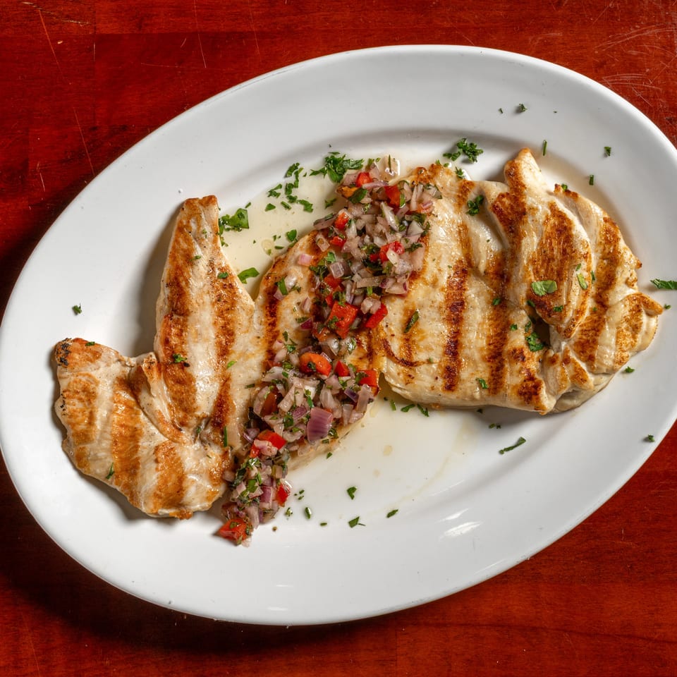 Grilled chicken breast topped with fresh pico de gallo and parsley on a white plate.
